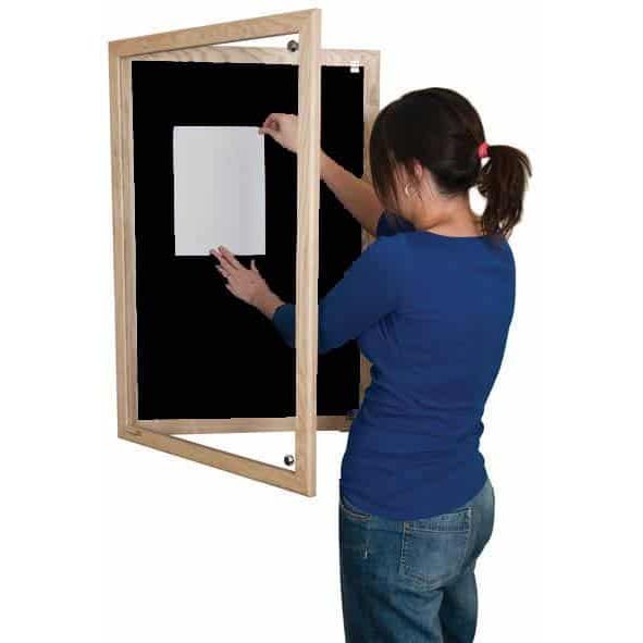 woman putting up a poster on a black lockable noticeboard