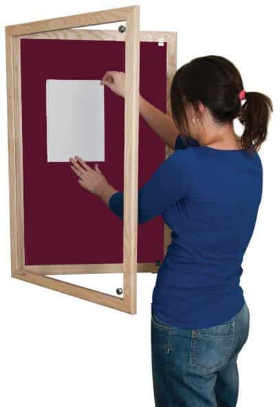 woman putting up a poster on a red lockable noticeboard