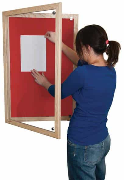 woman putting up a poster on an orange lockable noticeboard