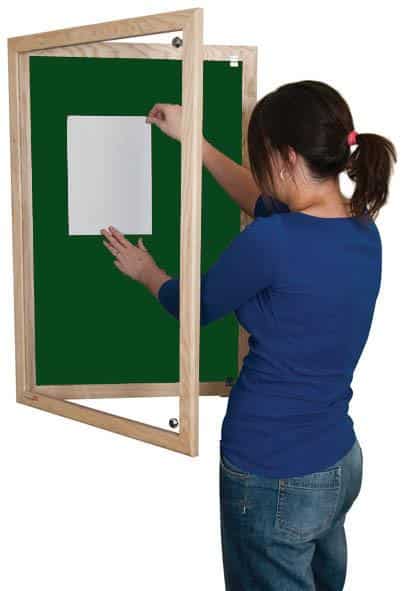 woman putting up a poster on a green lockable noticeboard