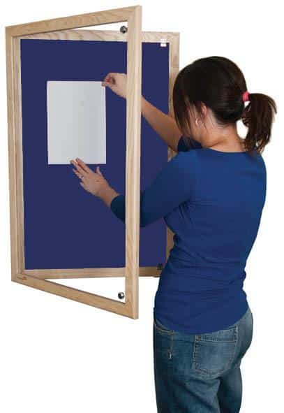 woman putting up a poster on a blue lockable noticeboard