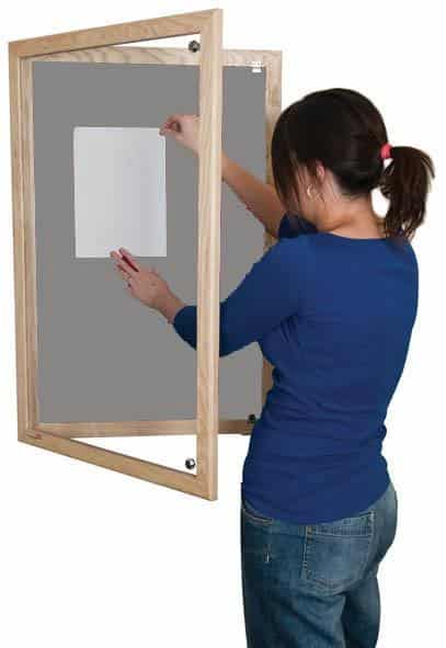 woman putting up a poster on a grey lockable noticeboard