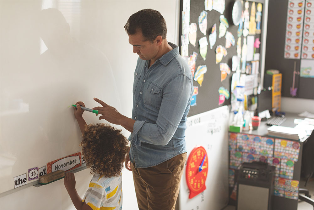 Man and child writing on whiteboard in a classroom setting