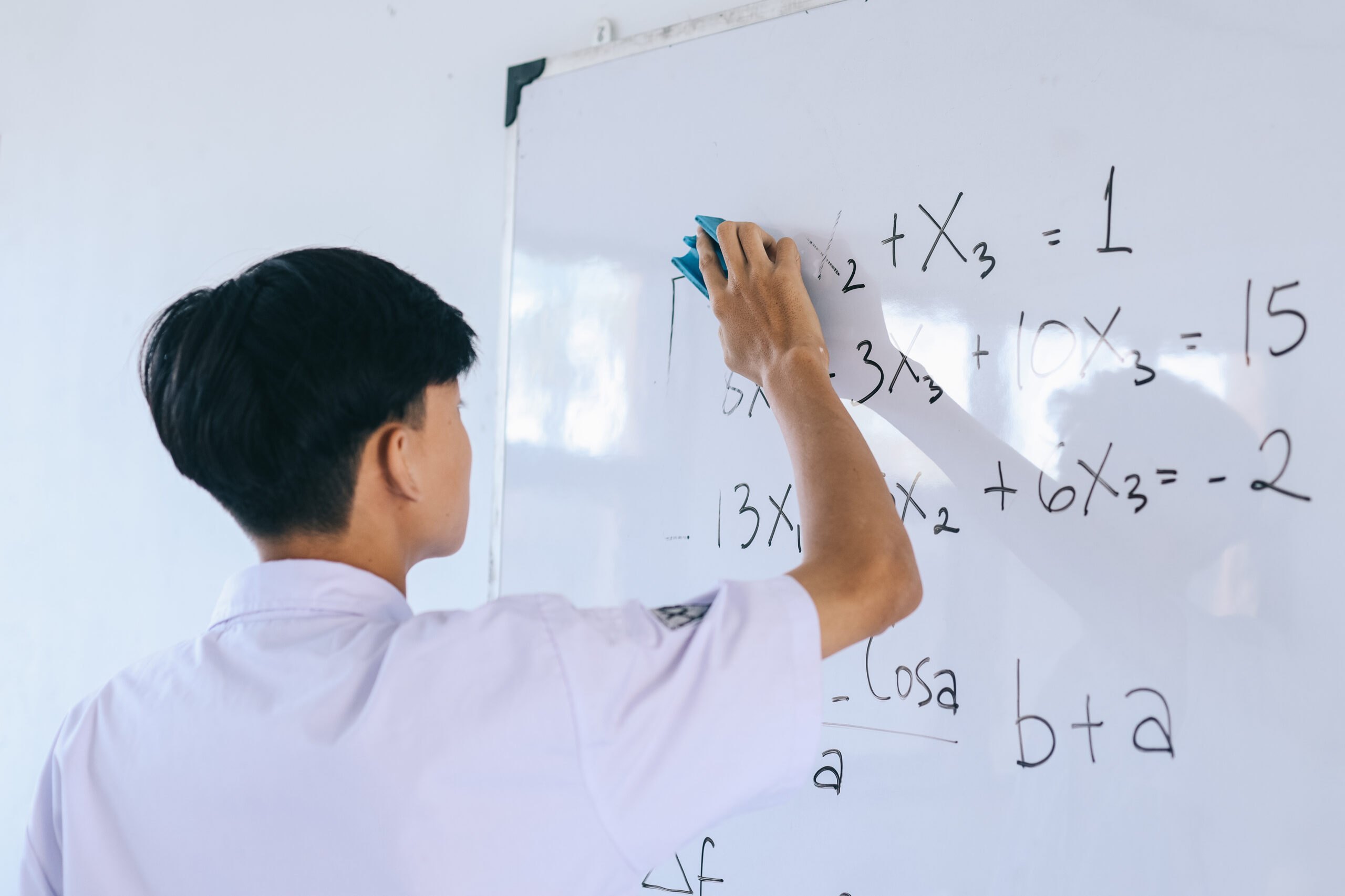 student cleaning whiteboard with maths problems on the page